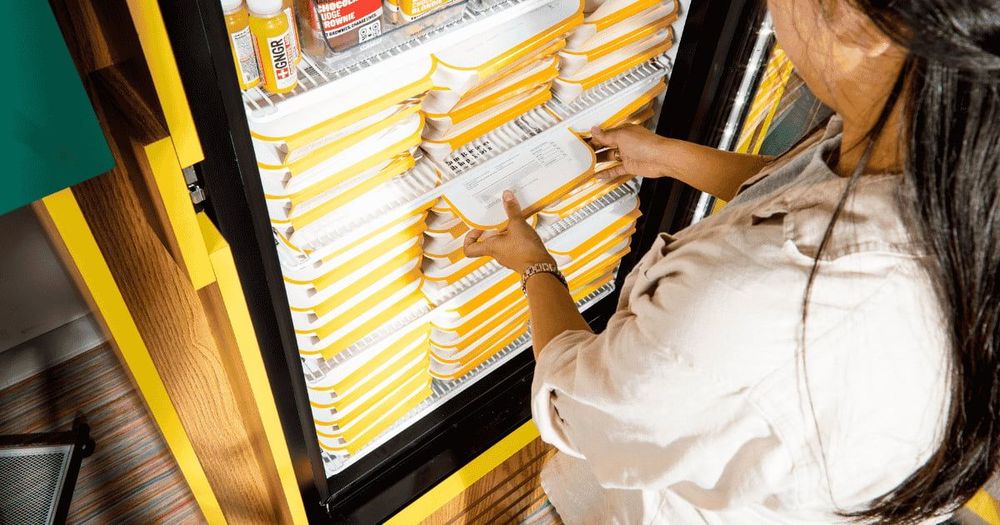 Resident selecting a fresh CookUnity chef-prepared meal from a fully stocked smart fridge in an apartment building